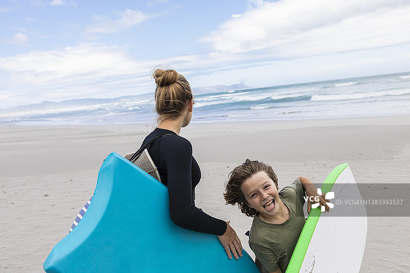 女孩（16-17岁）和男孩（8-9岁）在石窟海滩上拿着趴板图片素材