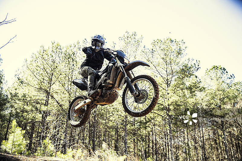 越野摩托车手在林地跳跃并指向相机图片素材