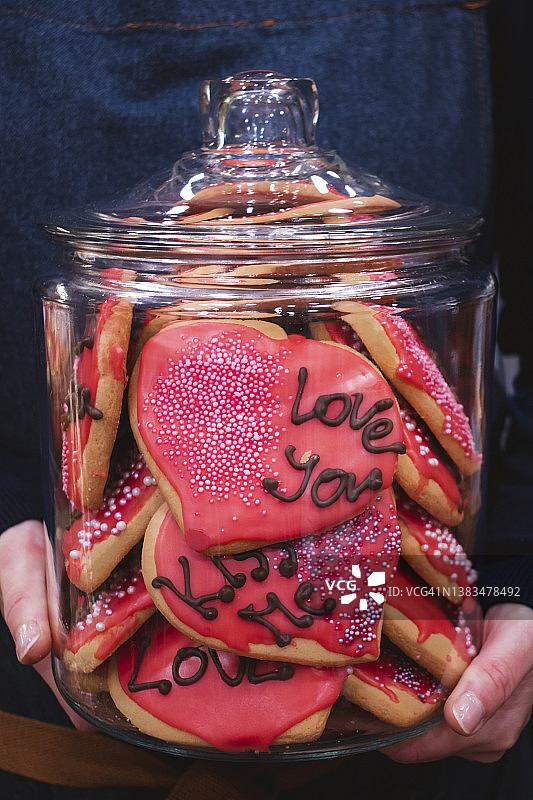 手拿装满心形饼干的玻璃罐，上面写着“爱你”和“吻我”图片素材