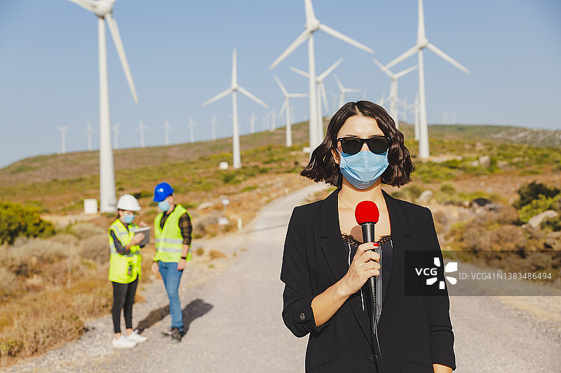 戴着口罩的女电视新闻记者在大流行期间报道可再生能源图片素材