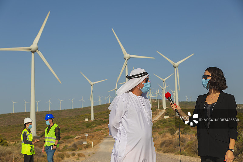 记者采访阿拉伯商人关于风力涡轮机可再生能源，新闻业，直播概念图片素材