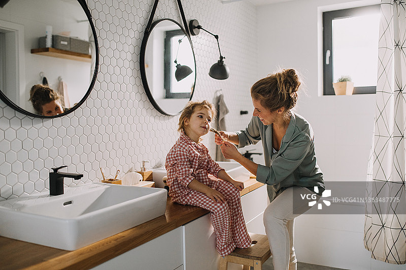 早晨，在家中浴室里，母亲给小女儿编辫子图片素材