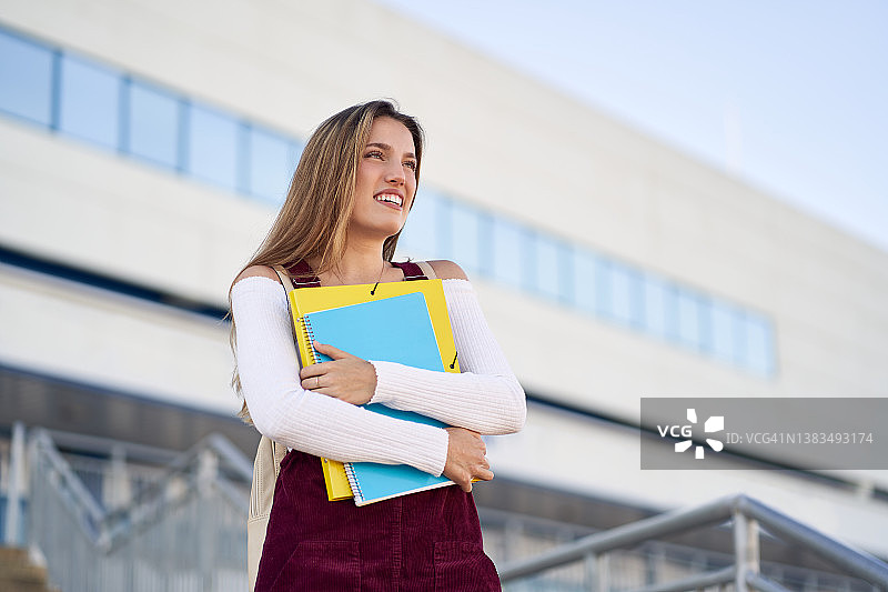 在大学附近拿着文件夹和笔记本的微笑女人图片素材