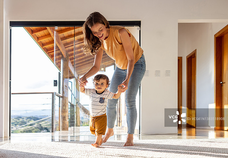 在家中母亲帮助下学习走路的幼儿图片素材