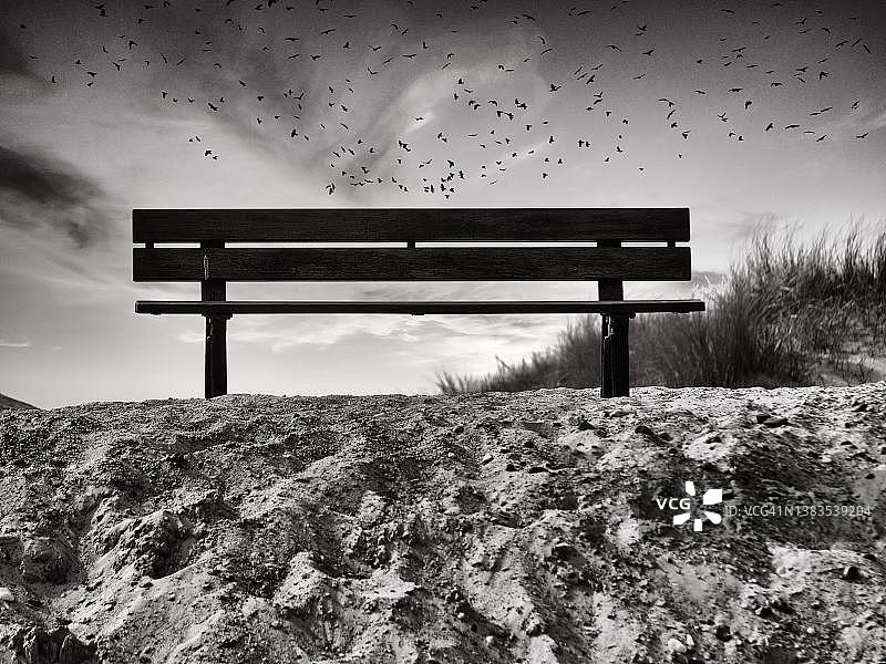 德国石勒苏益格-荷尔斯泰因州黑尔戈兰岛沙丘上的长椅，傍晚天空中有鸟群图片素材