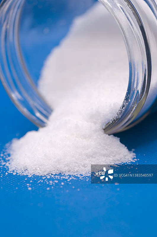 蓝色背景上从透明玻璃罐中洒出的盐图片素材