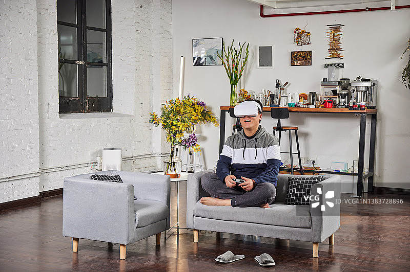 东亚男人戴VR眼镜在沙发上玩游戏图片素材