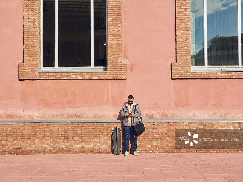 穿着休闲装、拿着笔记本电脑包和滑板的商务人士在上班路上打电话。另类出行方式。图片素材