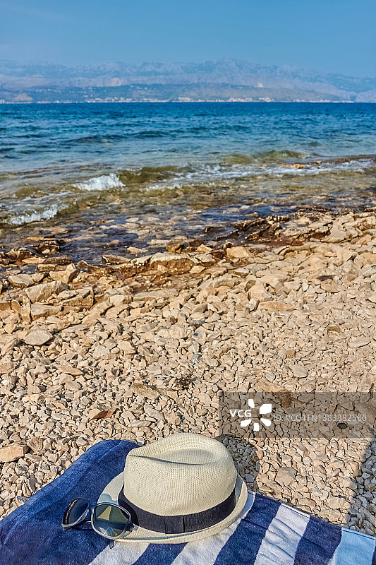 躺在鹅卵石海滩毛巾上的带太阳镜的帽子图片素材