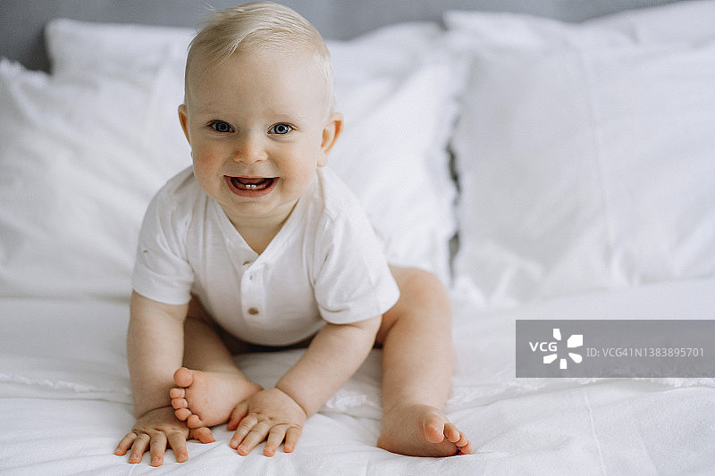 快乐的金发男婴坐在床上图片素材