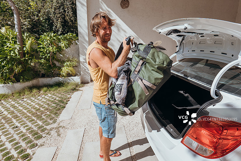 男人打包行李准备旅行，将行李装到汽车后备箱图片素材