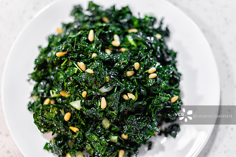 白色盘子上绿色羽衣甘蓝素食沙拉的扁平顶视图，配有松子和橄榄油背景图片素材