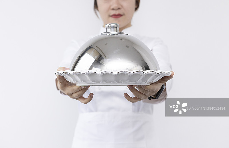 戴着厨师帽、手捧圆顶托盘和空盘子的亚洲女厨师宣传素材图片素材