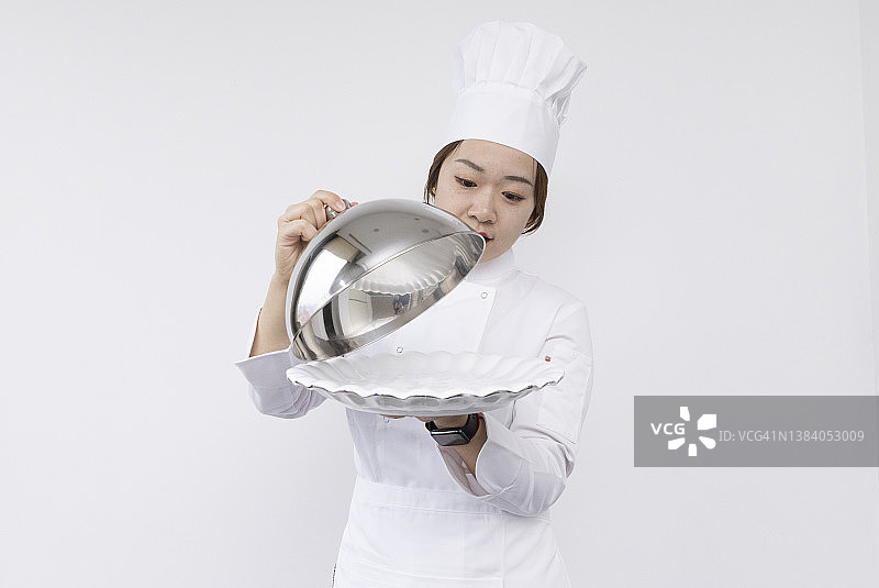 戴着厨师帽、手捧圆顶托盘和空盘子的亚洲女厨师宣传素材图片素材