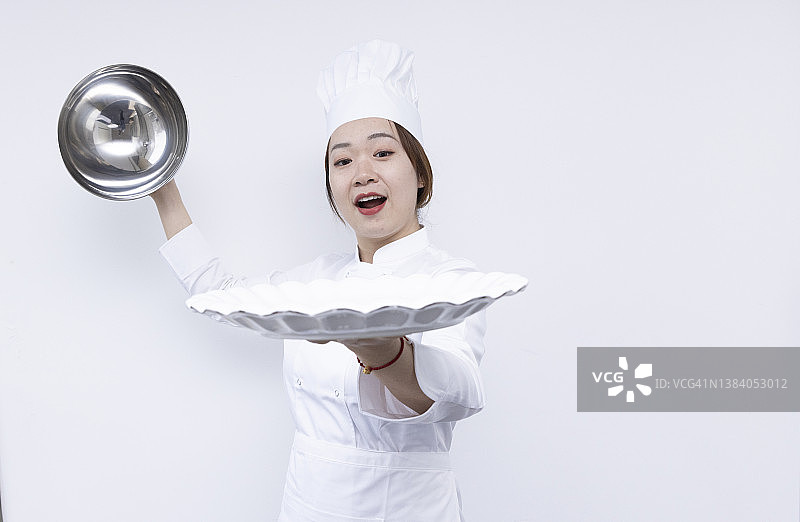 戴着厨师帽、手捧圆顶托盘和空盘子的亚洲女厨师宣传素材图片素材