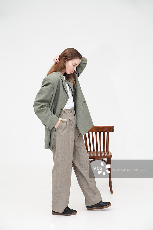 穿着超大号衣服站在旧椅子附近的沉思女人图片素材