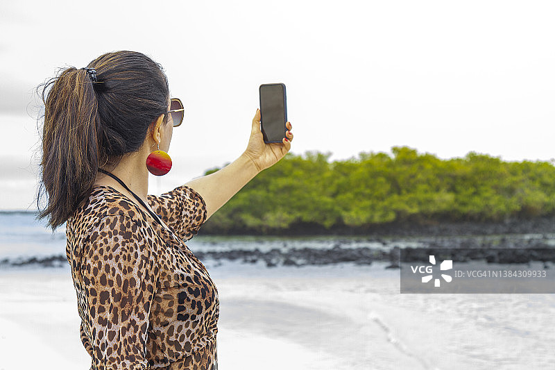 一位美丽的年轻女子在旅行,放松,探索,并用她的智能手机通过5G技术在加拉帕戈斯群岛的托图加湾给她的朋友们发送照片图片素材