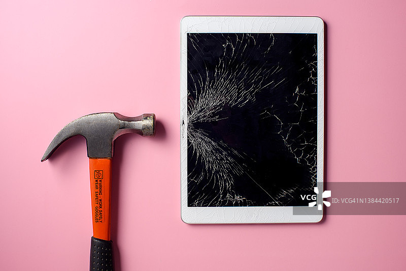 粉色背景上用锤子砸碎平板电脑图片素材