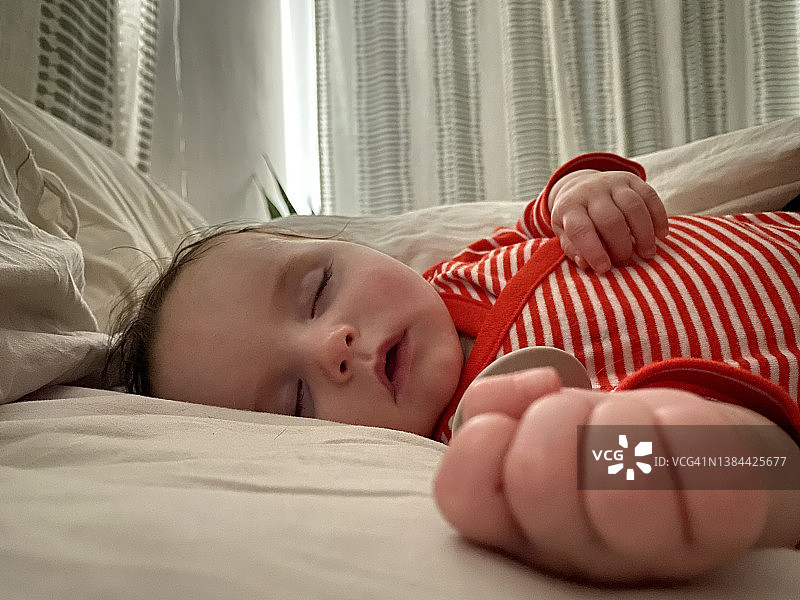 婴儿安睡在父母床上，手里拿着奶嘴仰视拍摄图片素材