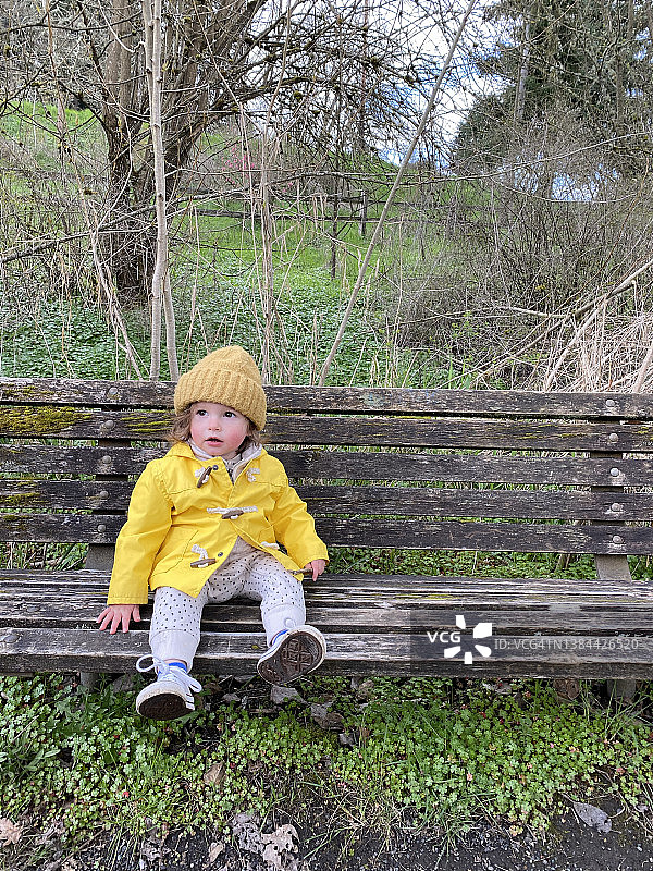 穿着黄色雨衣和帽子坐在破旧木凳上的幼儿女孩图片素材