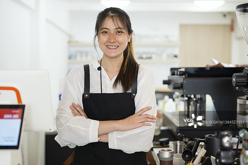 我们已准备好为您提供咖啡，亚洲女咖啡师站在咖啡店柜台前，双手交叉的肖像图片素材
