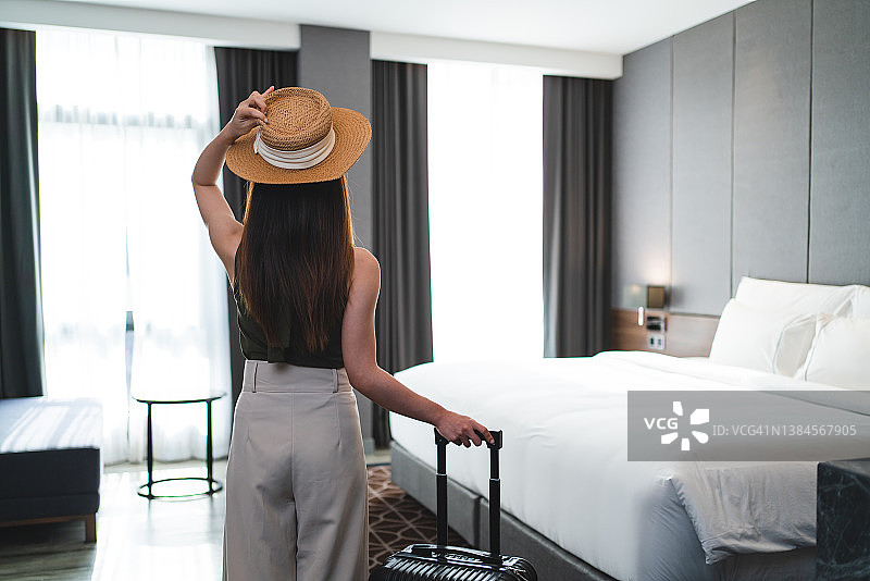 女子在酒店房间里办理入住手续的背影，手提行李箱图片素材