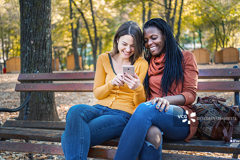 不同种族的朋友在秋天的公园里玩手机图片素材