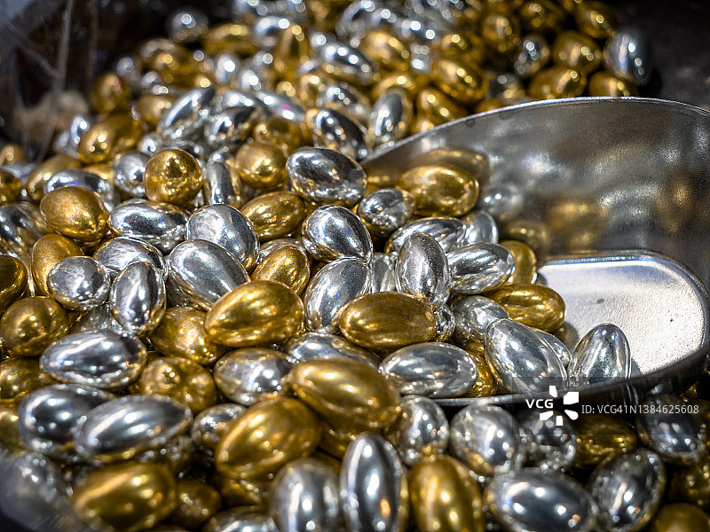 装满自选勺子的奢华美味银色和金色巧克力糖果球、豆子和坚果的微距特写。甜点和糖果瘾图片素材