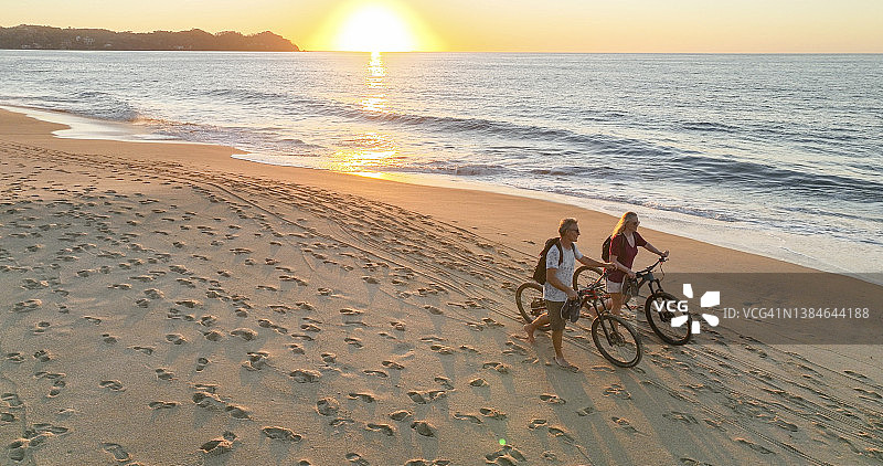 海滩上推自行车的夫妇鸟瞰图图片素材