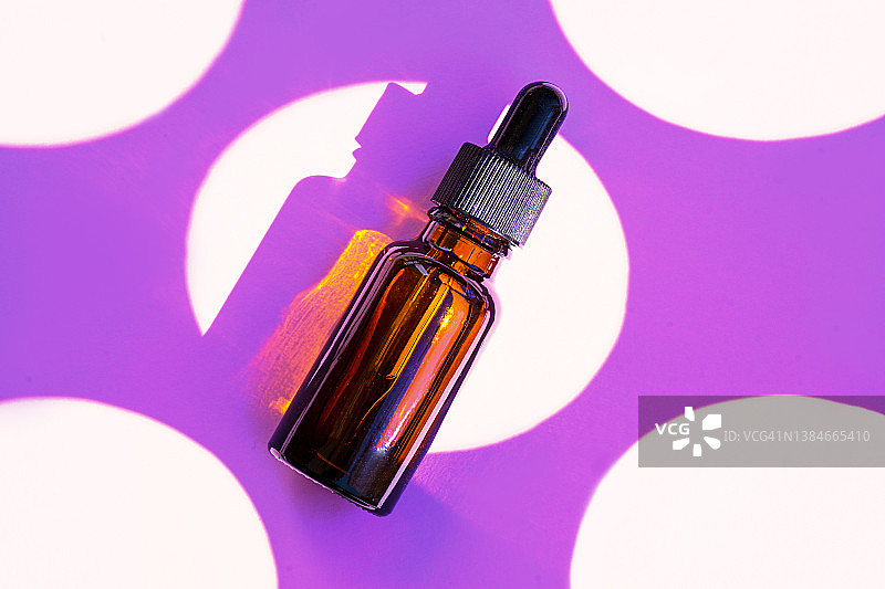 紫色背景上的面部精华或精油化妆品瓶特写，带有氧气气泡图片素材