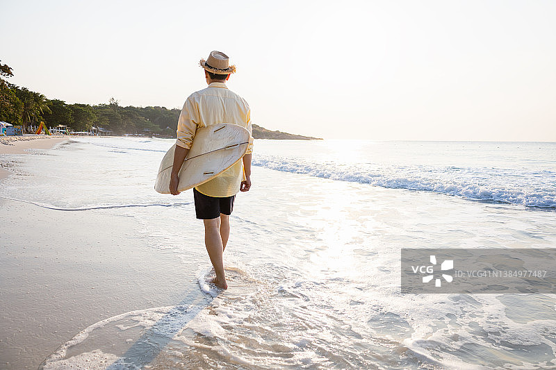 日出或日落时分，冲浪者在海边沙滩上拿着冲浪板行走。图片素材