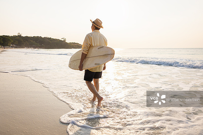 男人拿着专业冲浪板在日落长廊享受周末爱好，运动型男冲浪者在暑假期间行走图片素材