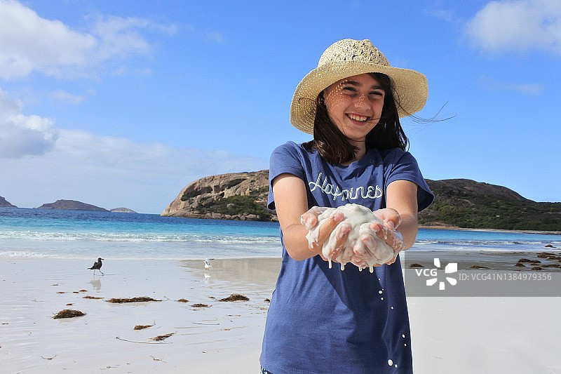 快乐的澳大利亚女孩在海滩上捧着沙子图片素材