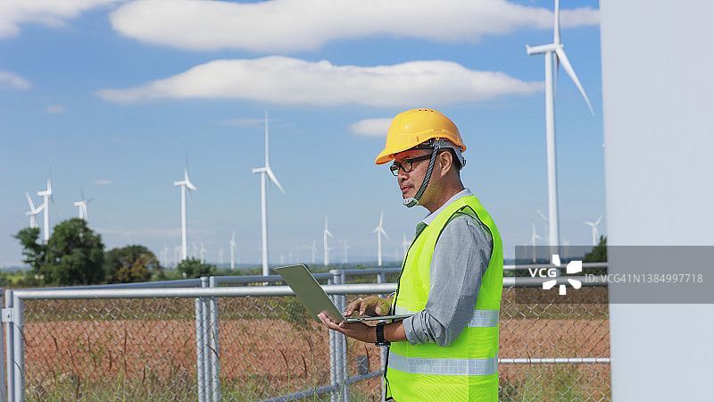 工程师在风力涡轮机现场使用笔记本电脑发电，用于可再生能源、清洁能源或环境保护概念图片素材