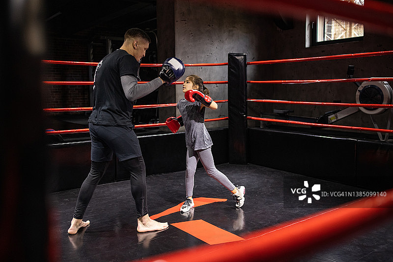 健身俱乐部内，小女孩在男教练的指导下练习跆拳道图片素材