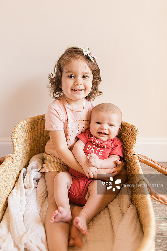 34个月大的女童在情人节抱着她2个月大的弟弟坐在编织的 Moses 篮子里图片素材