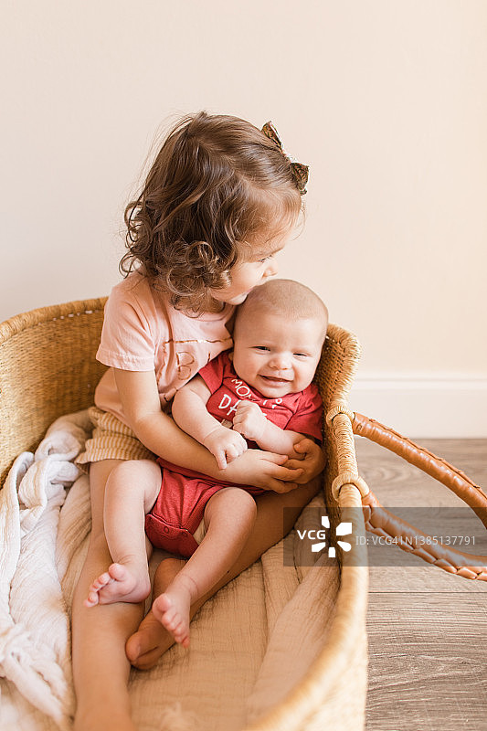 34个月大的女童在情人节抱着她2个月大的弟弟坐在编织的 Moses 篮子里图片素材