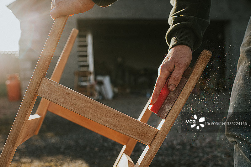 男人用砂块打磨木制椅架图片素材