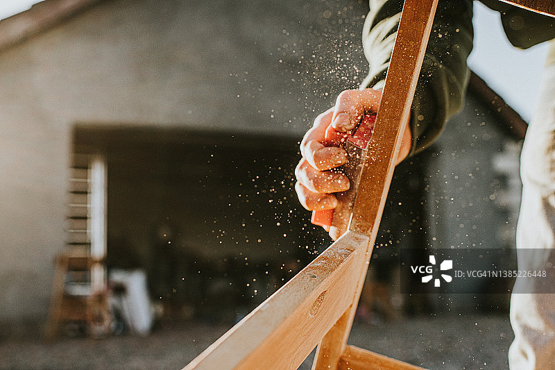 男人用砂块打磨木制椅架图片素材