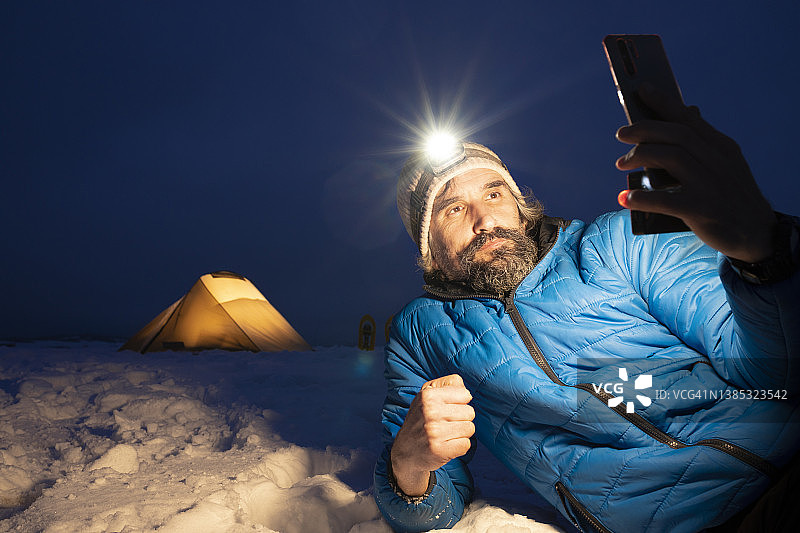 独自在冬季山中露营的游客晚上用手机图片素材