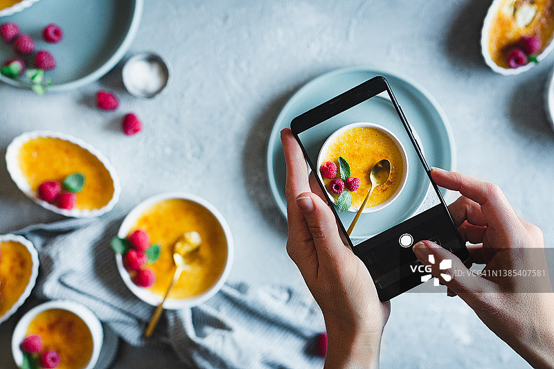 女人用手机拍摄新鲜制作的焦糖布丁图片素材