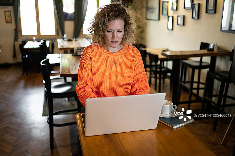 在现代咖啡馆用笔记本电脑工作的白人自由职业女性图片素材