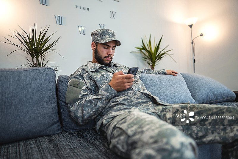 坐在客厅沙发上使用智能手机的士兵图片素材