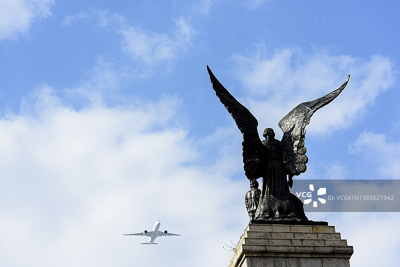 天使雕塑前的飞行飞机图片素材