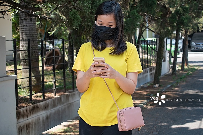 年轻亚裔女子戴着防护口罩在街上使用智能手机图片素材