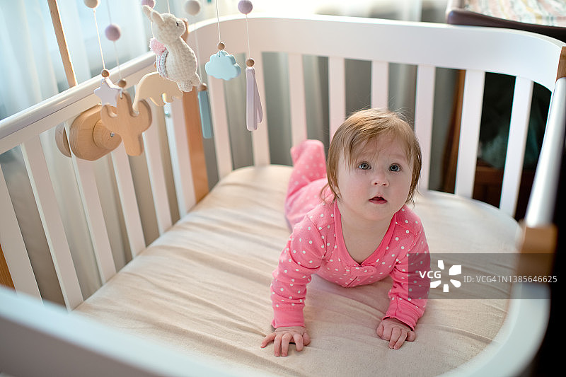 阳光明媚的早晨，快乐的粉红连体女婴在室内玩耍图片素材