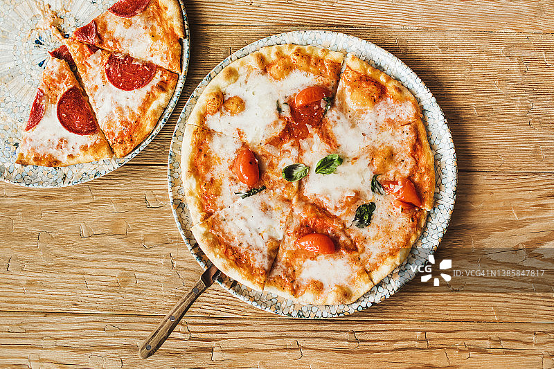 美味的现烤意大利辣香肠和玛格丽特披萨俯视图，配以木桌上的火腿，地中海文化图片素材