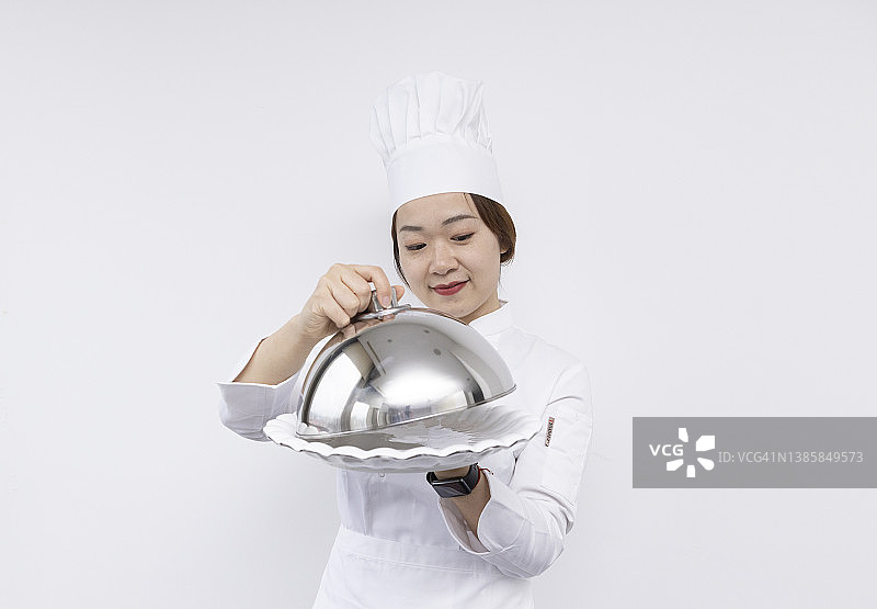 戴着厨师帽、手捧圆顶托盘和空盘子的亚洲女厨师宣传素材图片素材