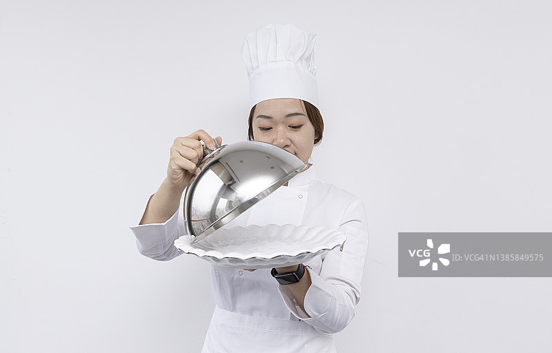 戴着厨师帽、手捧圆顶托盘和空盘子的亚洲女厨师宣传素材图片素材