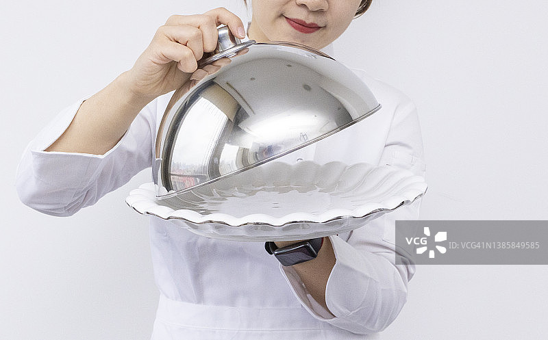 戴着厨师帽、手捧圆顶托盘和空盘子的亚洲女厨师宣传素材图片素材